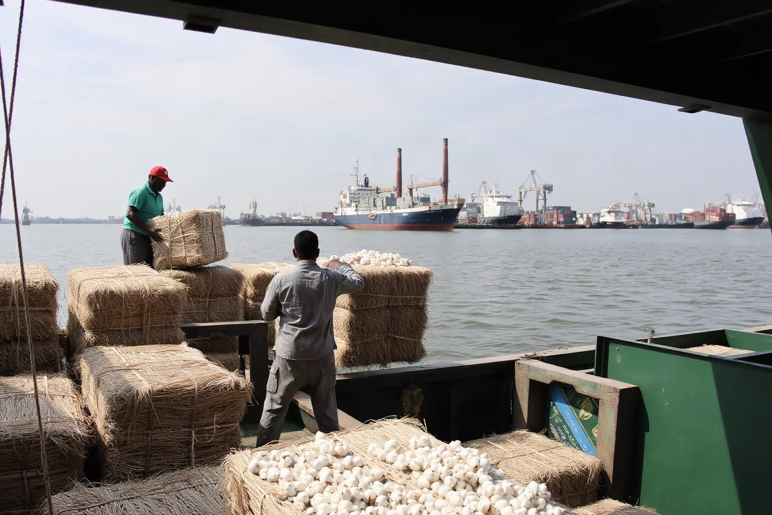 Dockworkers loading raw materials like cotton bales onto a ship bound for a factory port