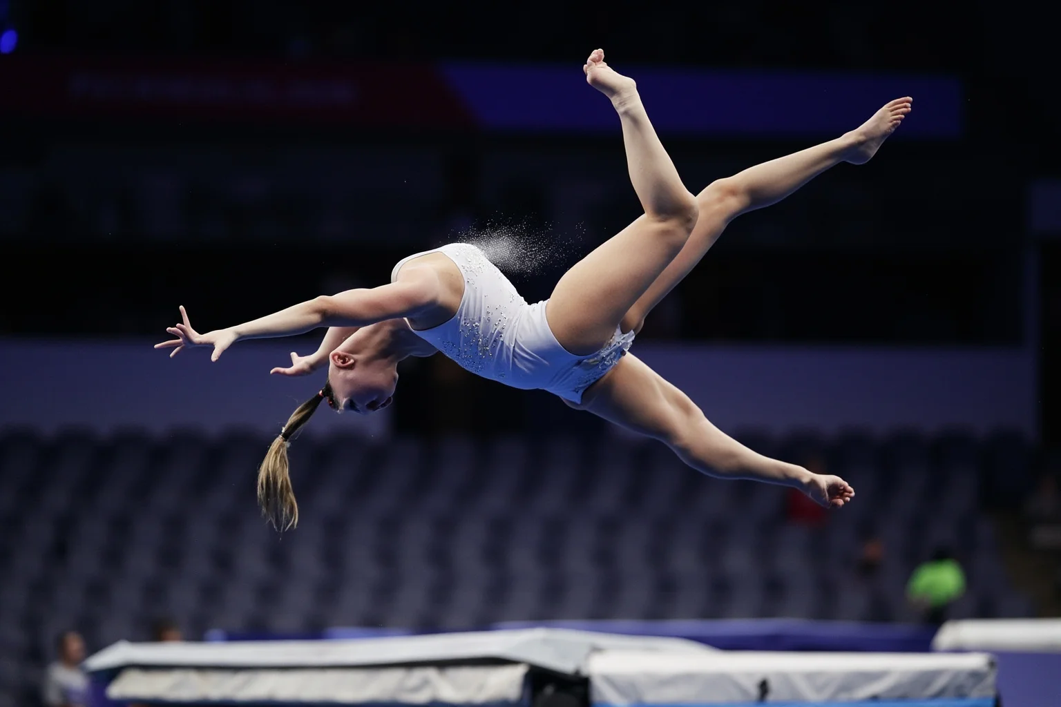 Female Athletes In History Who Changed The Game 23 Elite female gymnast frozen mid-air during a high-difficulty floor routine tumbling pass, chalk dust visible in bright arena lighting