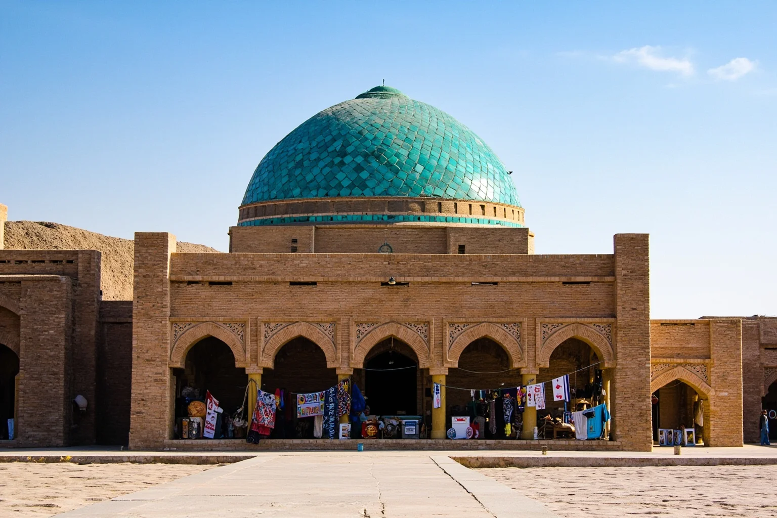 Exterior of a Silk Road domed trading hall in Bukhara with merchants selling crafts beneath a turquoise-tiled dome