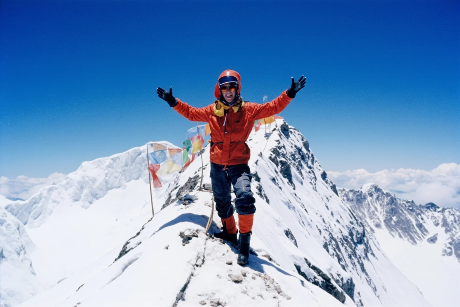 Female Athletes In History Who Changed The Game 14 Female mountaineer in bright 1970s expedition gear standing triumphantly on a snowy summit ridge with prayer flags