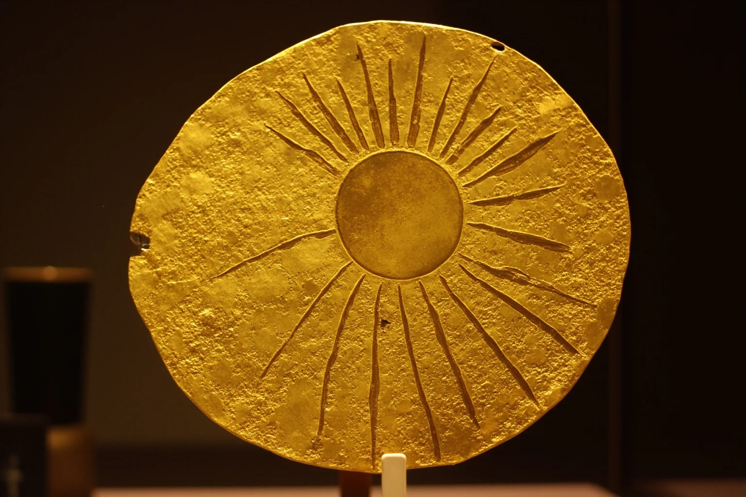Gold foil disc etched with sun and bird motif, ancient artifact on display