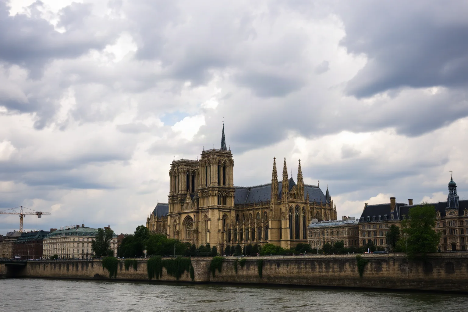 Gothic cathedral facade with flying buttresses and twin towers beside a river, dramatic cloudy sky, wide shot