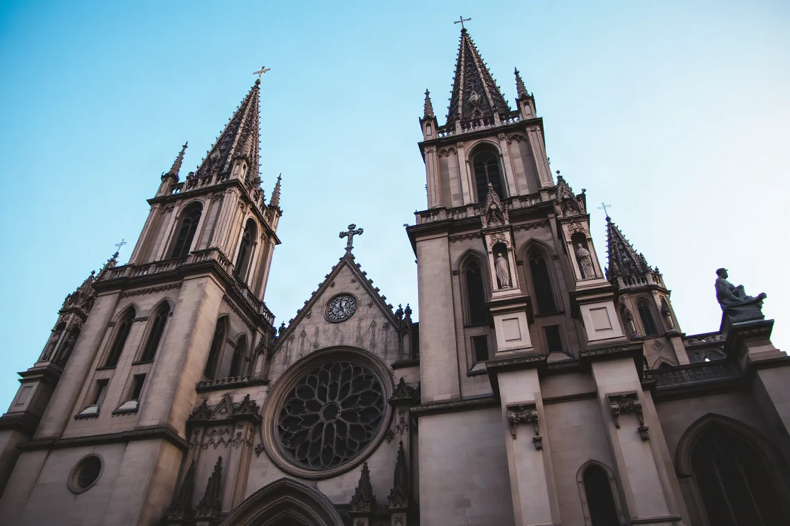 Gothic cathedral facade with twin spires and rose window, stone sculptures, soft blue evening sky