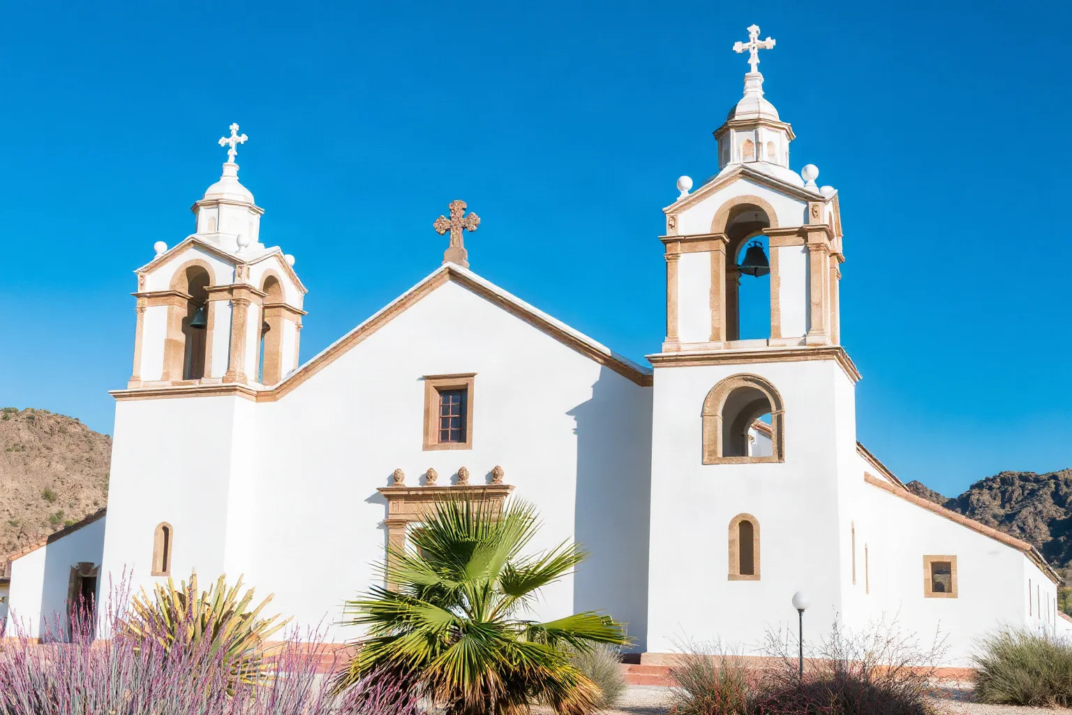 Grand white stucco Spanish mission church with ornate Baroque bell towers in a desert setting