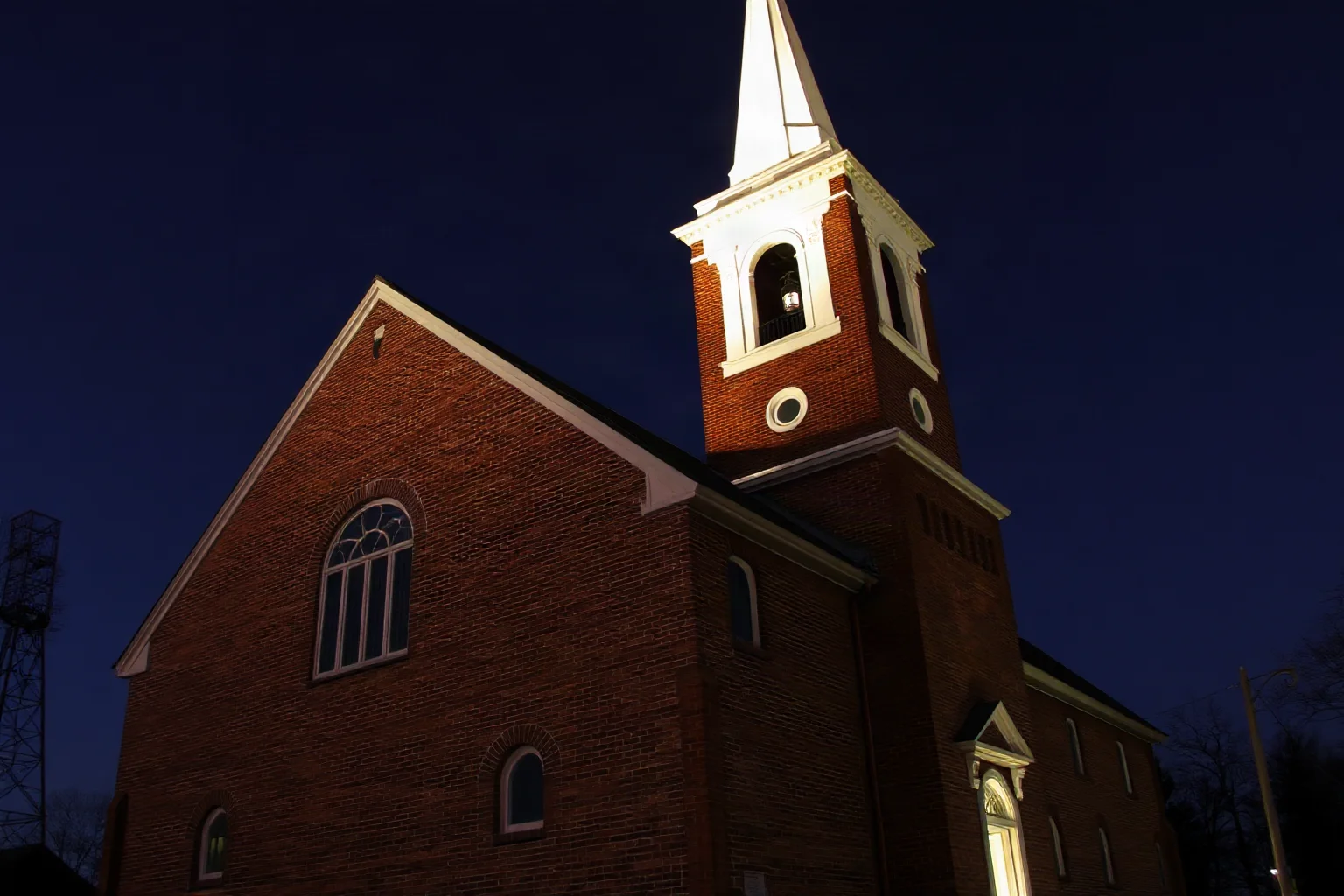 Historic brick church with a tall white steeple silhouetted against a night sky with lantern light in the tower