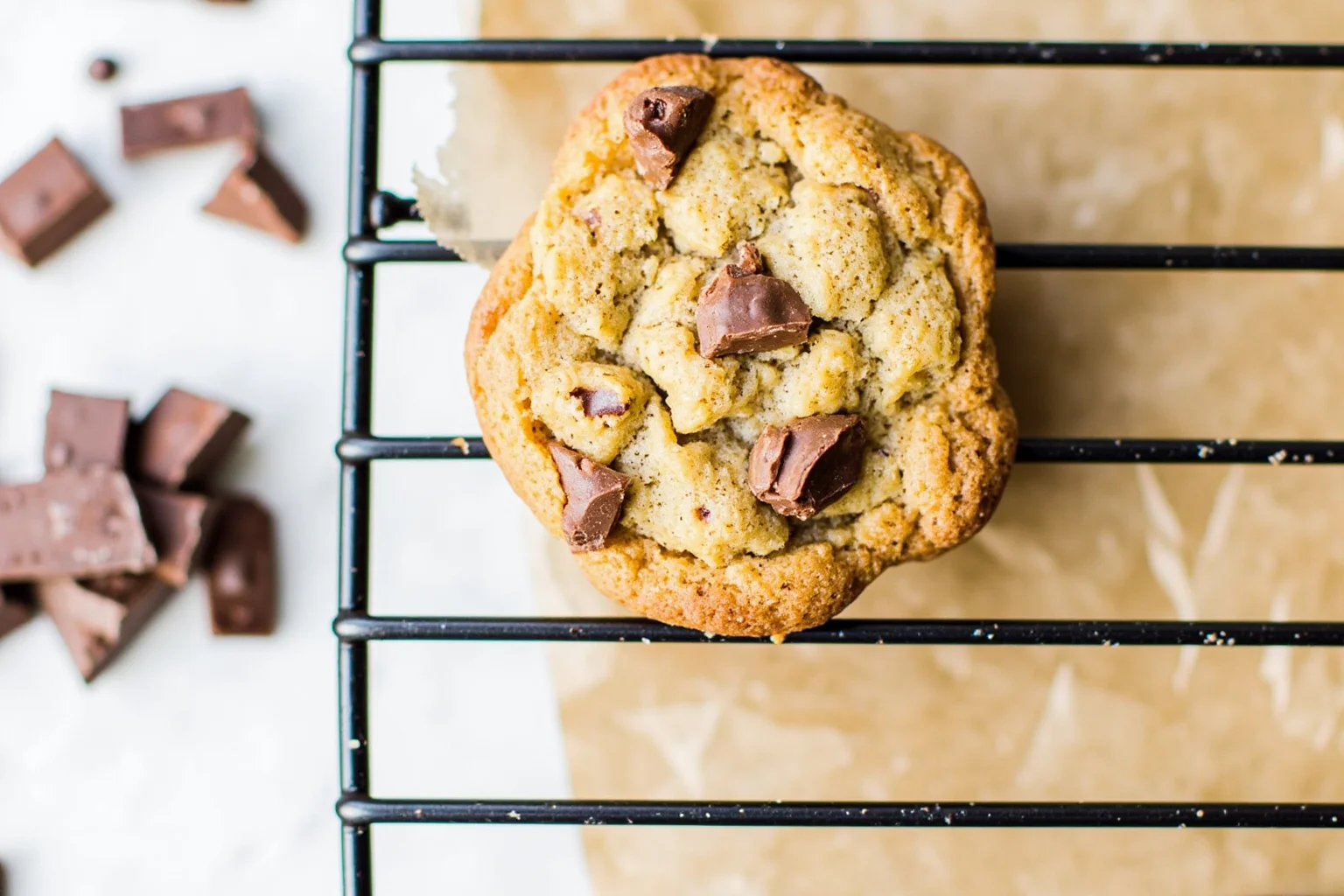 Homemade chocolate chip cookie on cooling rack with chocolate bar pieces nearby