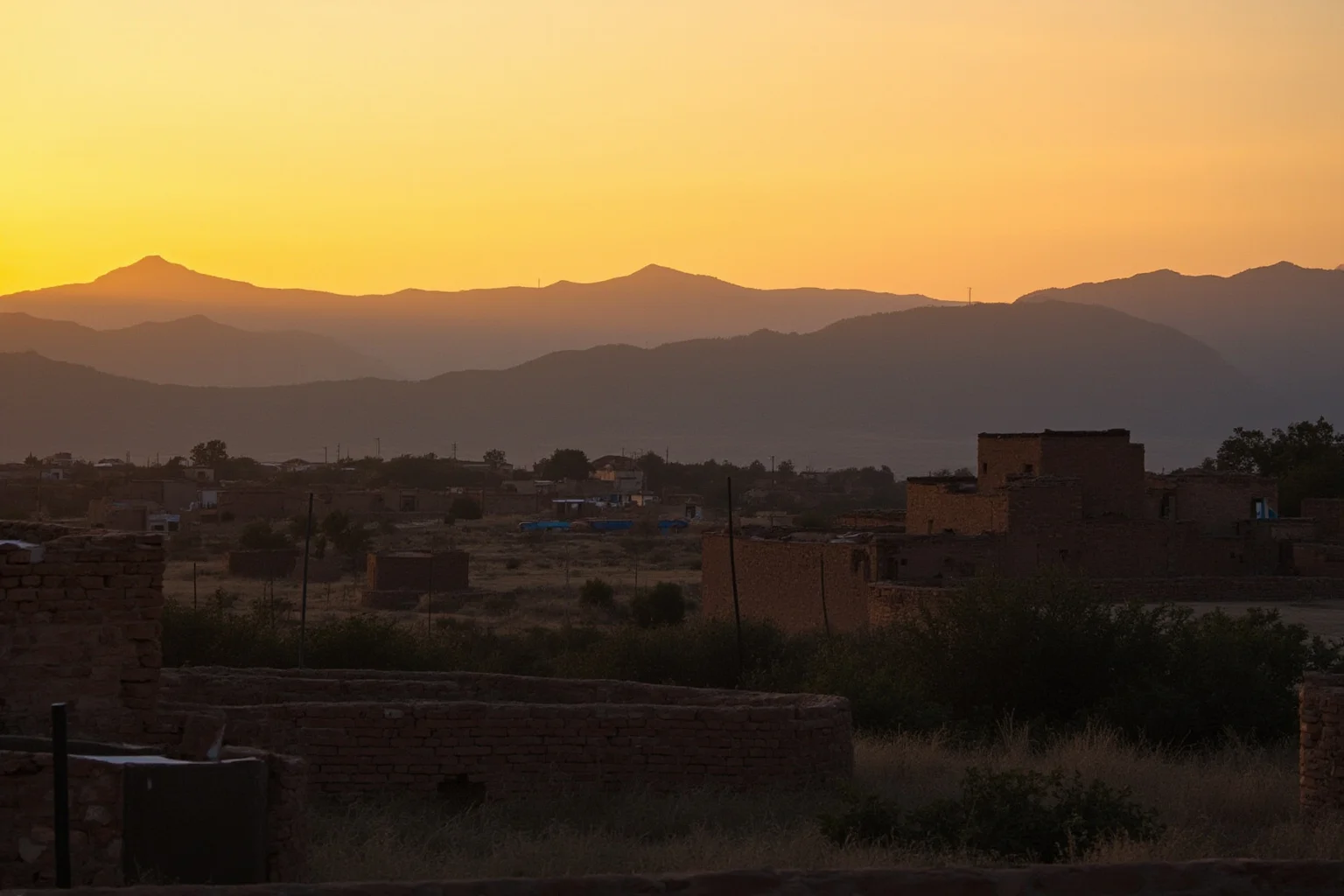 A rural village landscape in Sinaloa, Mexico at sunset with adobe buildings and mountains in the distance