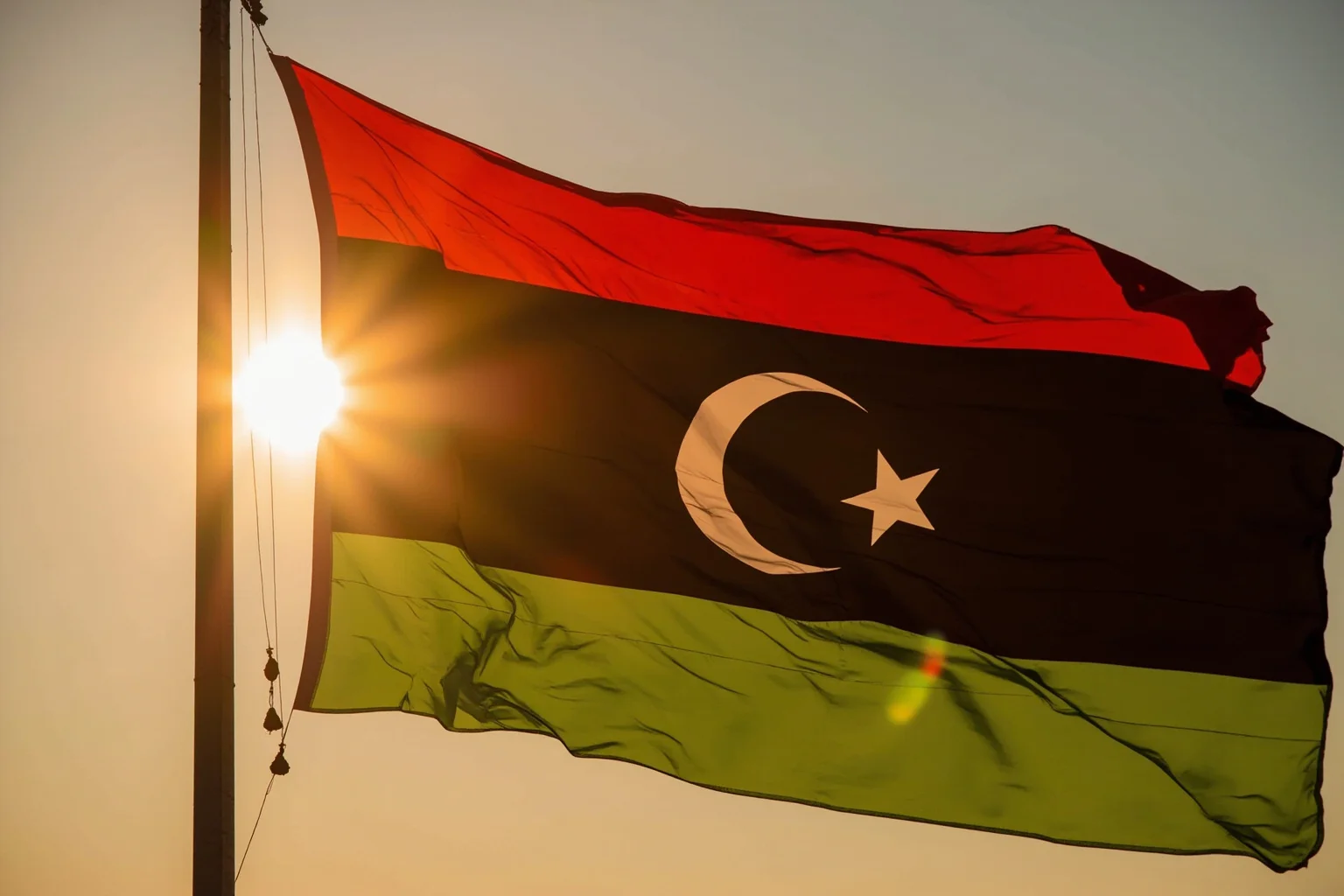 Libya's red, black, and green flag with white crescent and star, waving during a symbolic sunrise