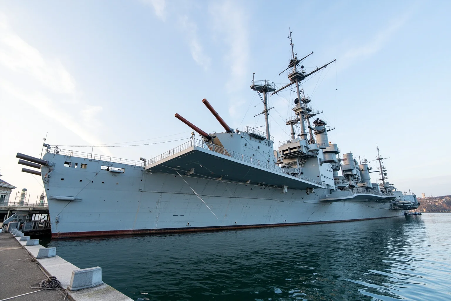 The Longest-Serving Warships of All Time 15 Massive World War II era battleship with enormous gun turrets and gray hull, docked as a museum beside a harbor pier