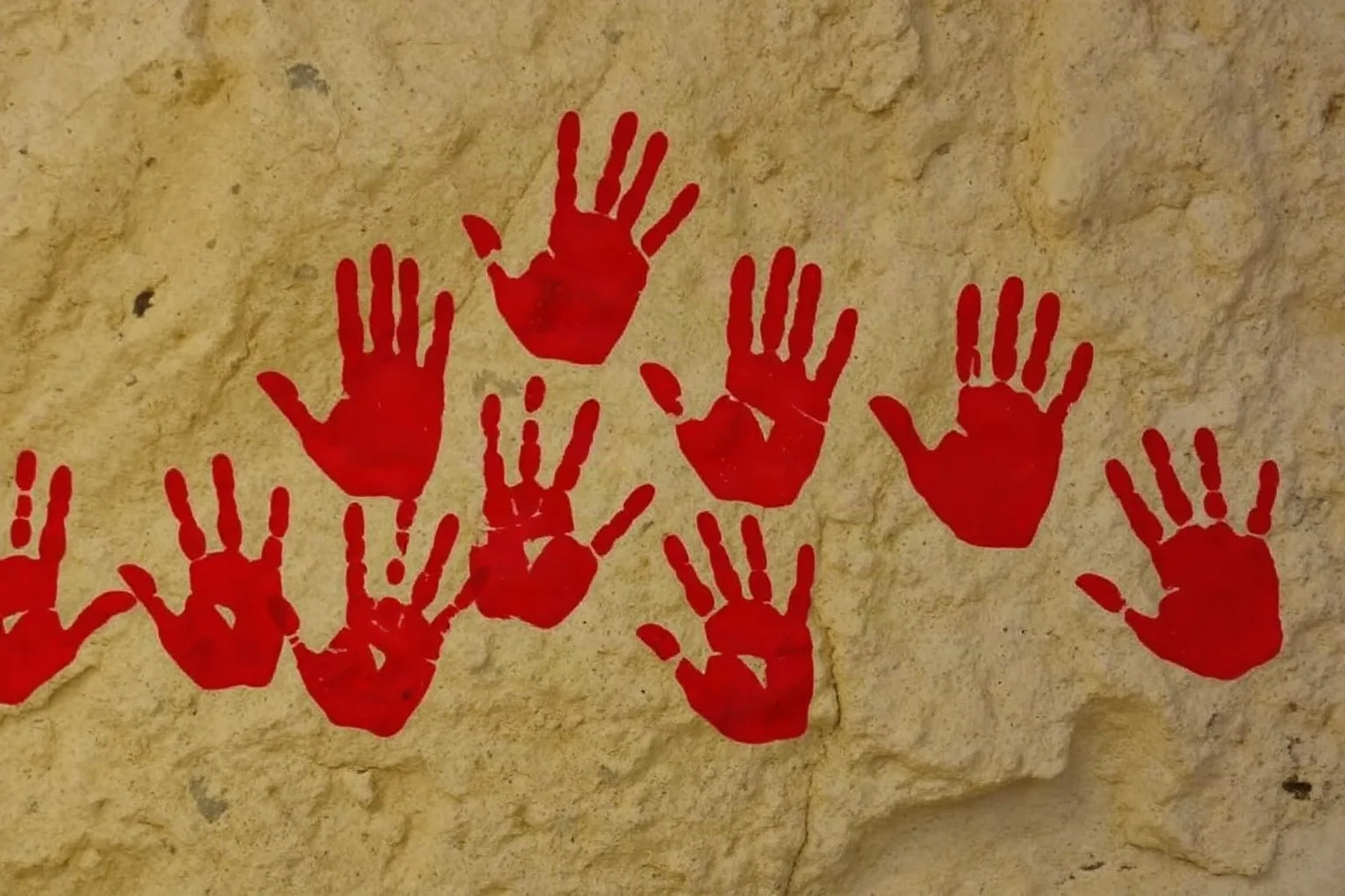 Multiple human hand stencils in red pigment on a cave wall created by blowing paint around pressed hands, overlapping prints