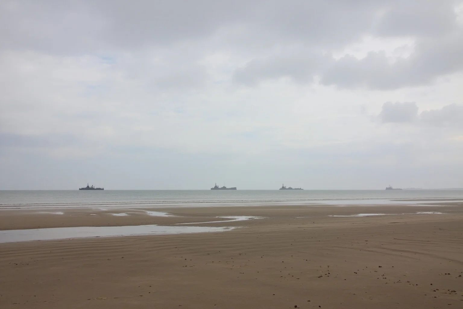 Best Nonfiction Books About WWI: The 25 Best WWI and WWII Reads 22 Normandy beach at low tide with distant landing craft silhouettes, overcast sky
