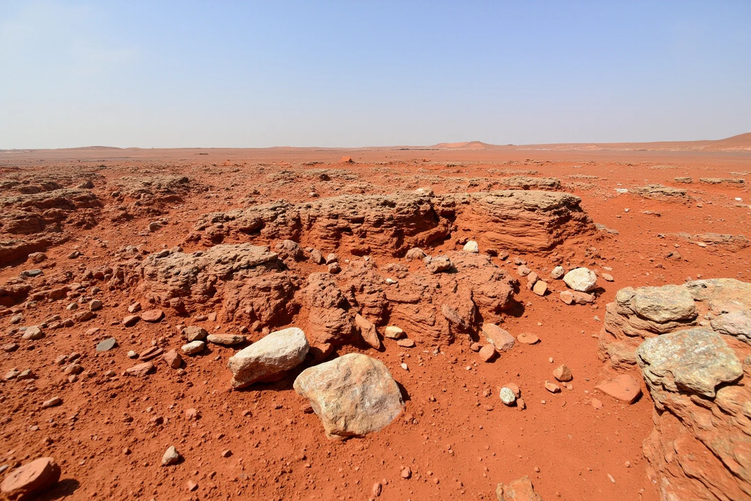 North African rocky desert terrain with layered reddish-brown sediment and distant dunes