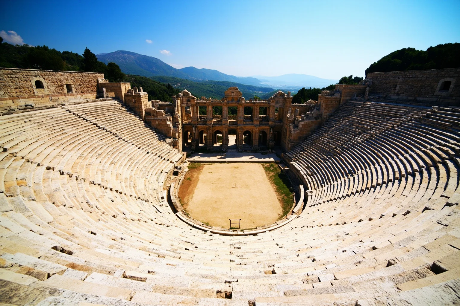 Panoramic view of the Ancient Theatre of Epidaurus in Greece, semi-circular limestone seating rows surrounded by green hills