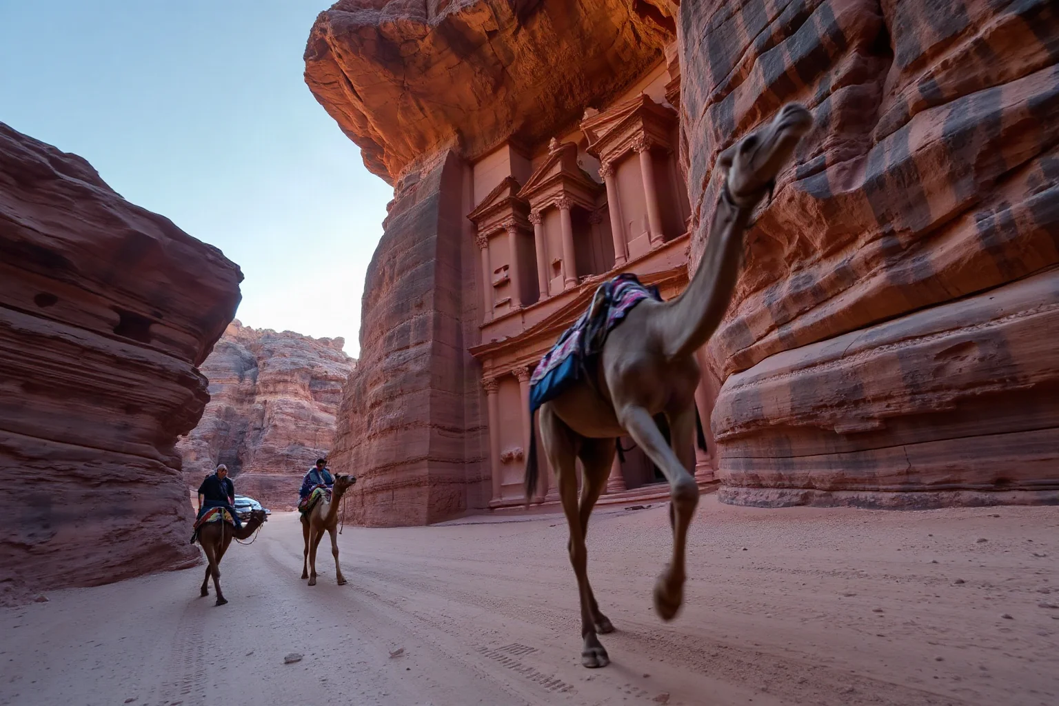 Rock-carved facade of a desert city resembling Petra at dawn, camel caravan approaching