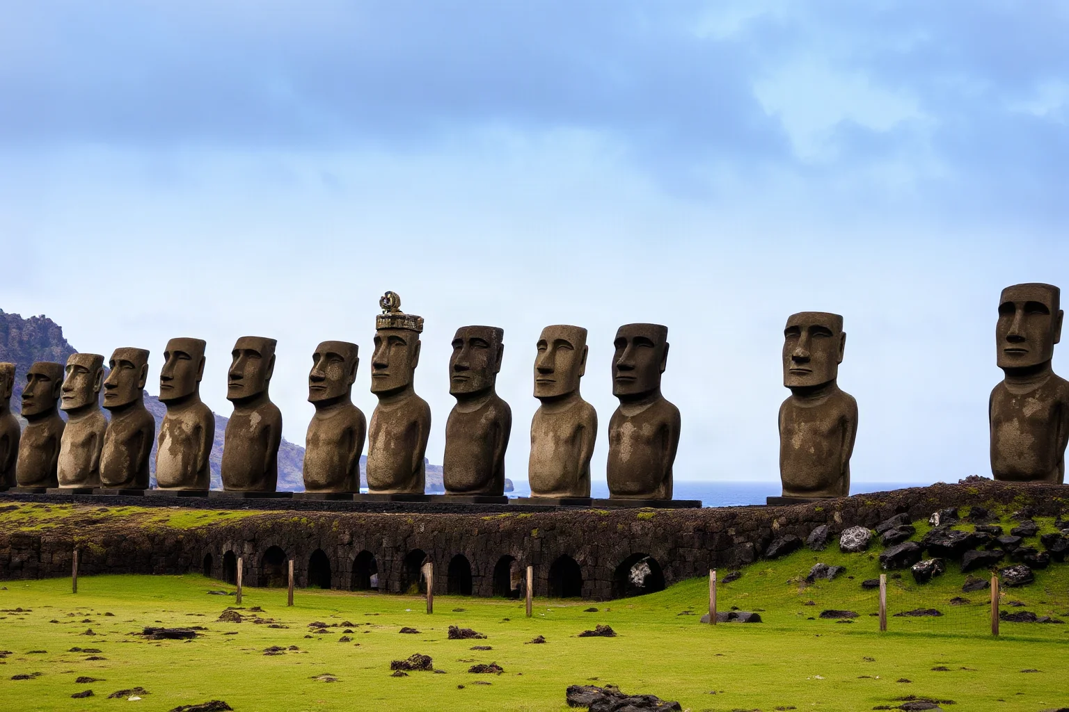 Rows of large stone head-and-torso statues standing along a grassy volcanic island coastline