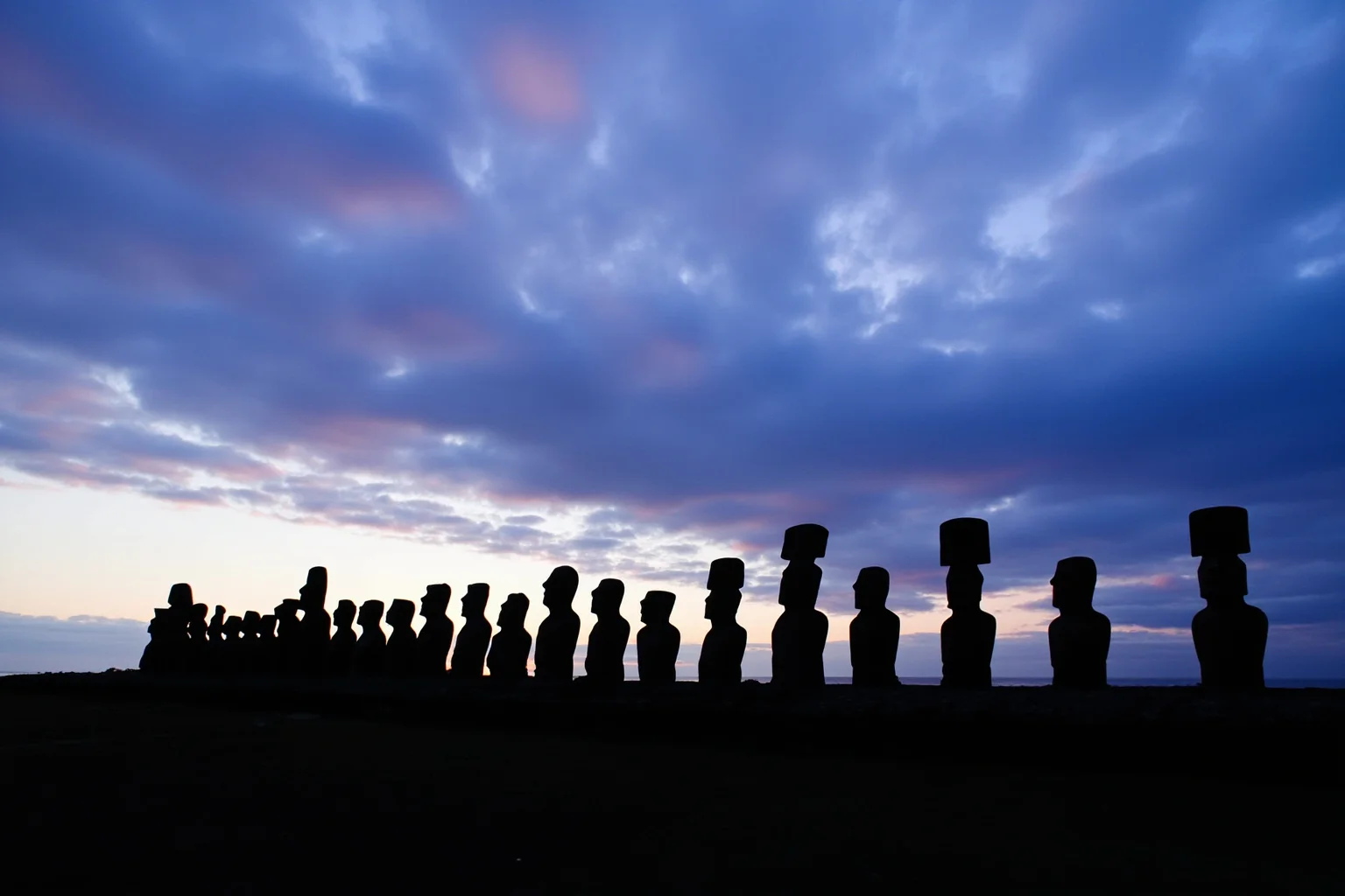 Rows of moai statues standing along the coastline of Easter Island at dusk