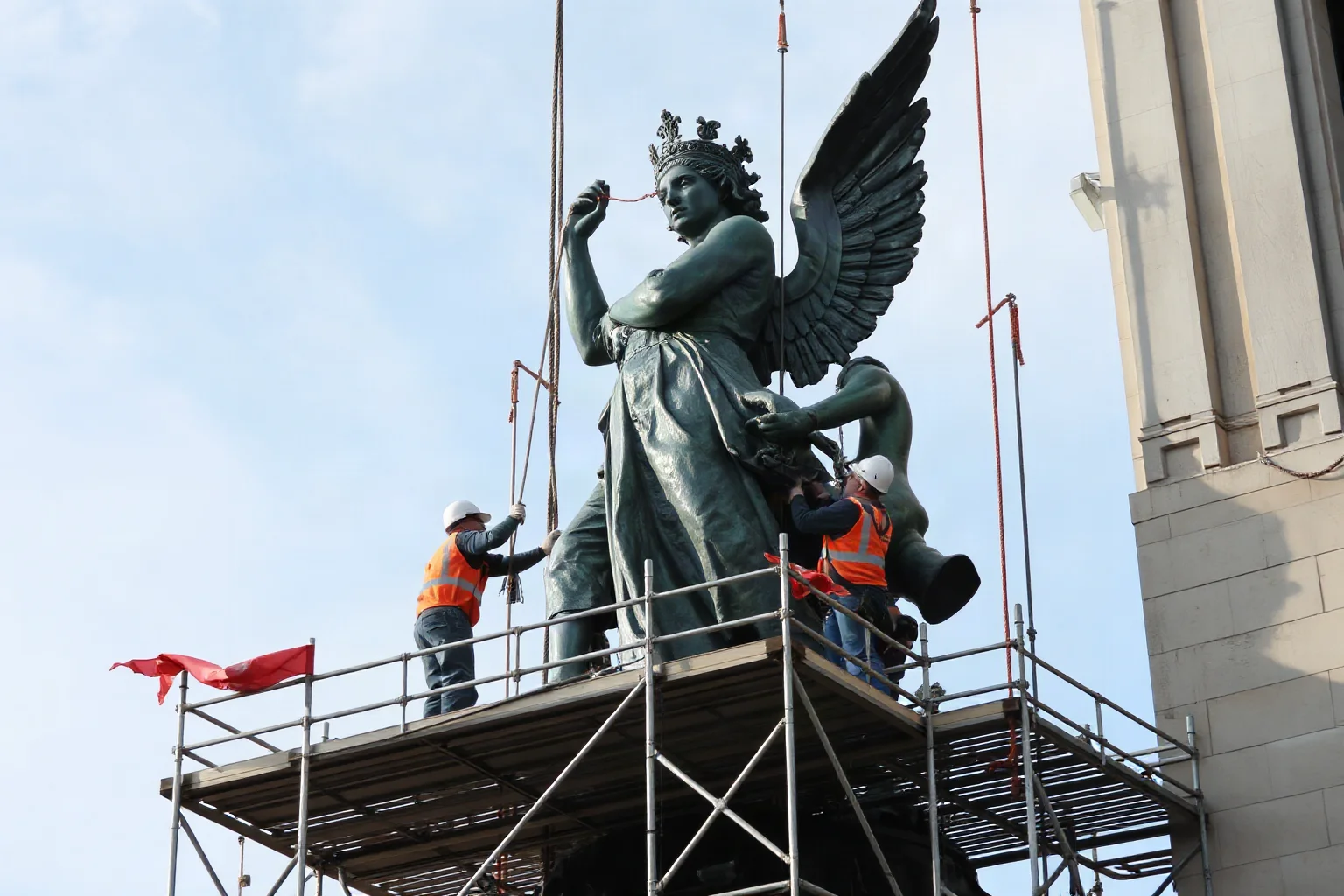 Scaffolding and restoration workers repairing a large copper statue, illustrative construction scene