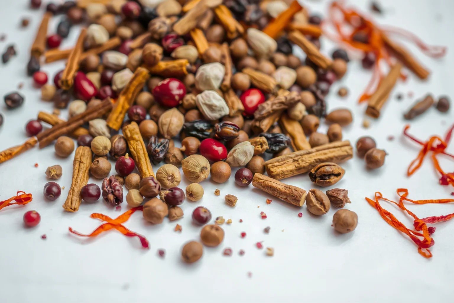 Scattered pile of exotic spices including peppercorns, cinnamon sticks, cloves, nutmeg, and saffron threads