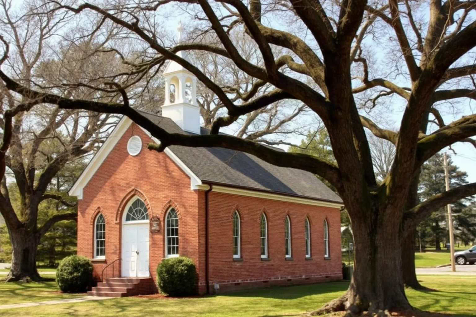 Simple colonial brick church with pointed Gothic arch windows surrounded by old oak trees in rural Virginia