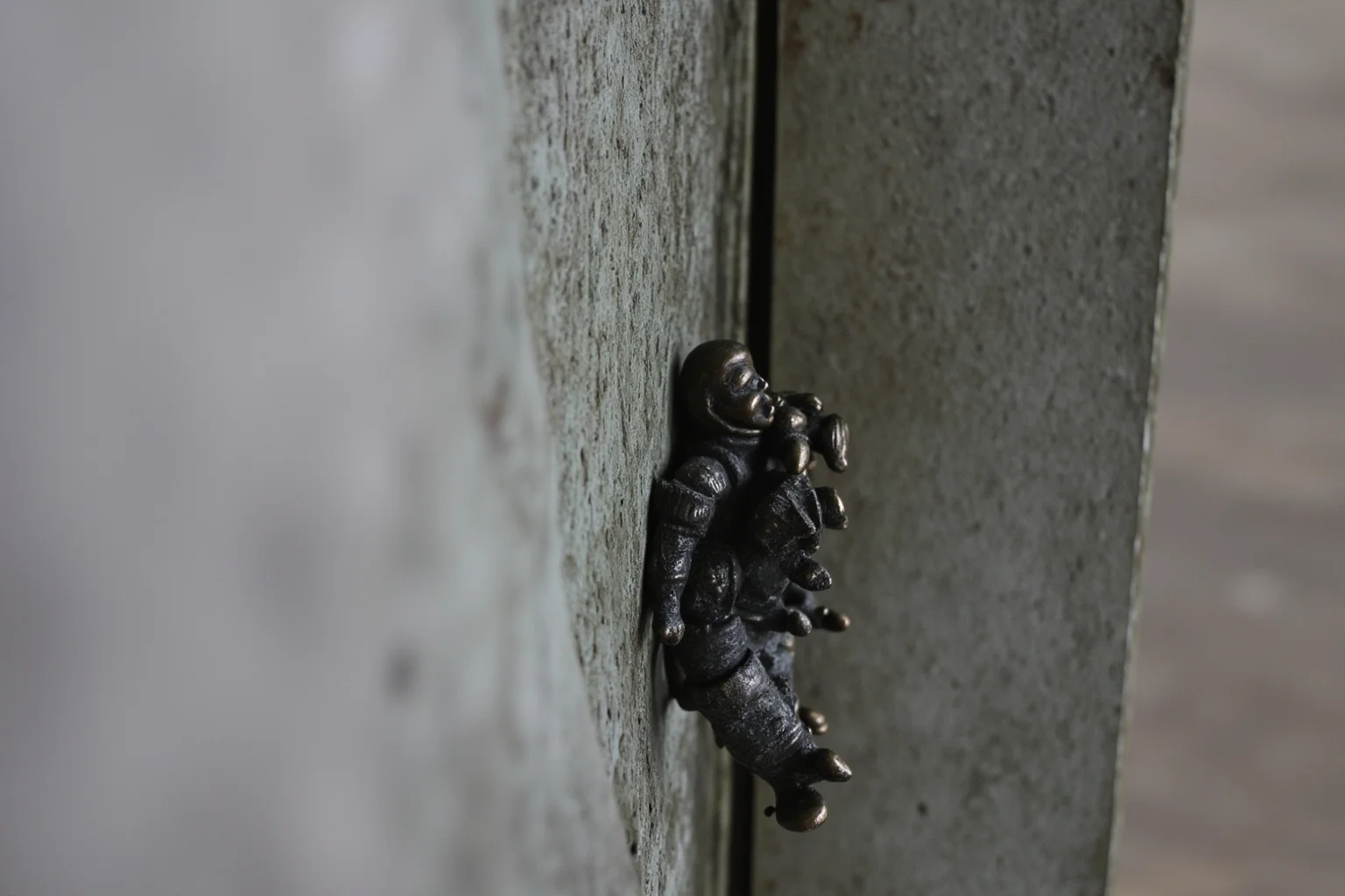 Small abstract bronze figures resembling astronauts tucked into the corner of a large sculptural relief