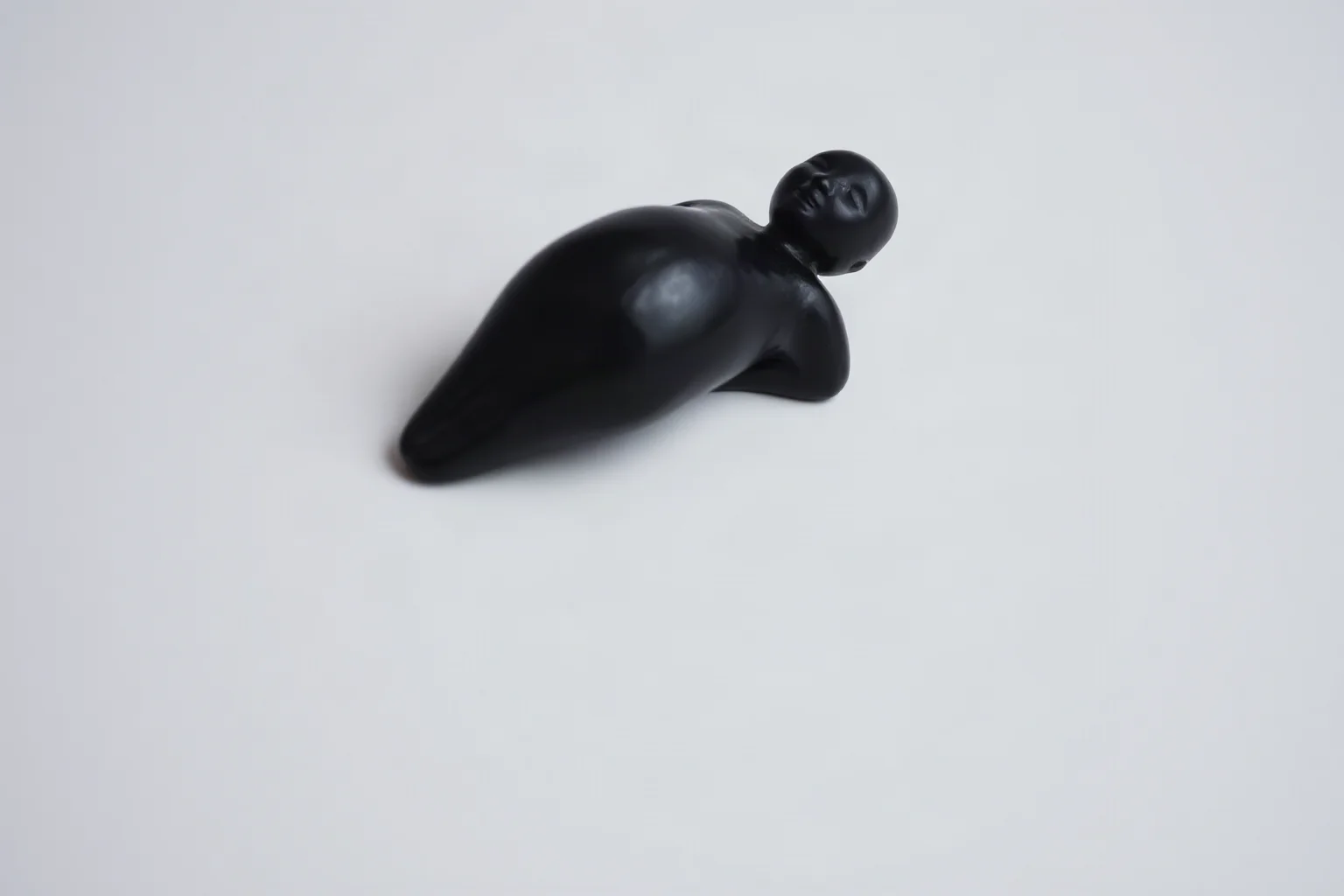 Small dark fired-clay figurine of a rounded human female form resting on a neutral surface