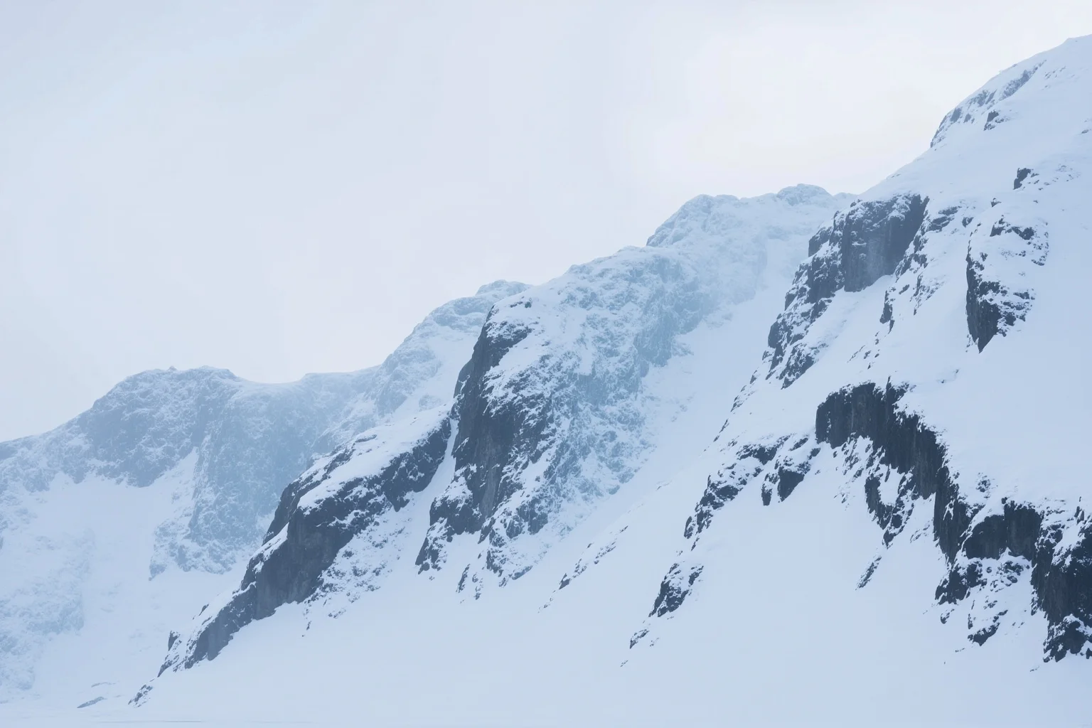 Snow and ice covered Antarctic mountainside with dark exposed rock ridges