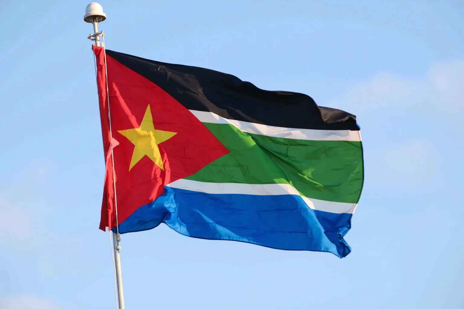 South Sudan's black, red, green, and blue flag with a gold star, waving proudly against a clear sky