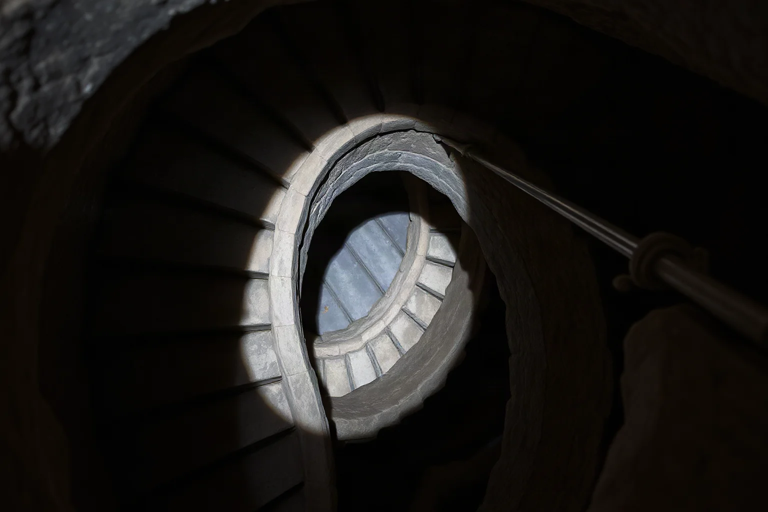 Spiral stone staircase descending approximately 20 meters underground into darkness, narrow and steep