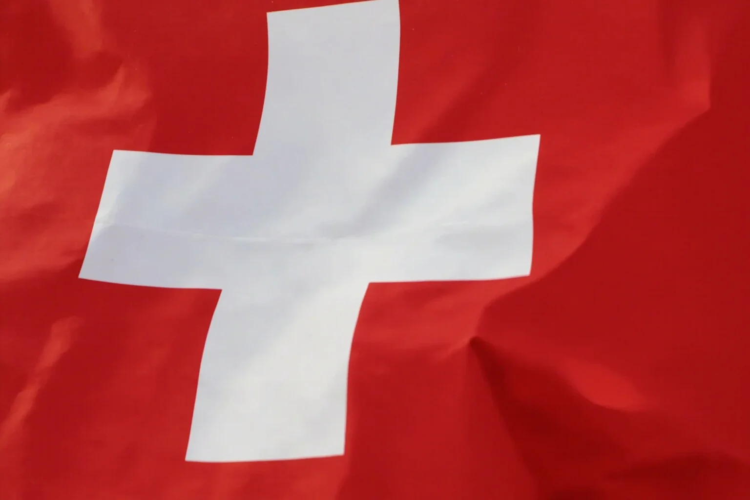Switzerland's white cross on red flag with a faint medieval shield pattern behind it