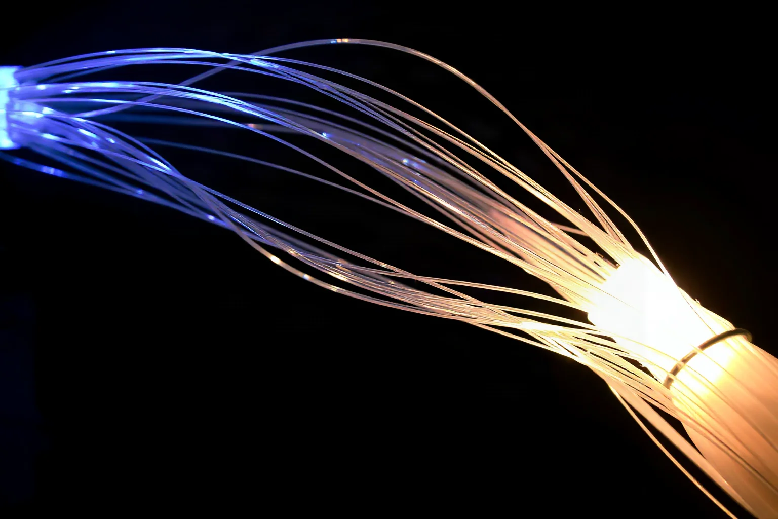 Thin glowing glass fiber strands bundled together on a dark background