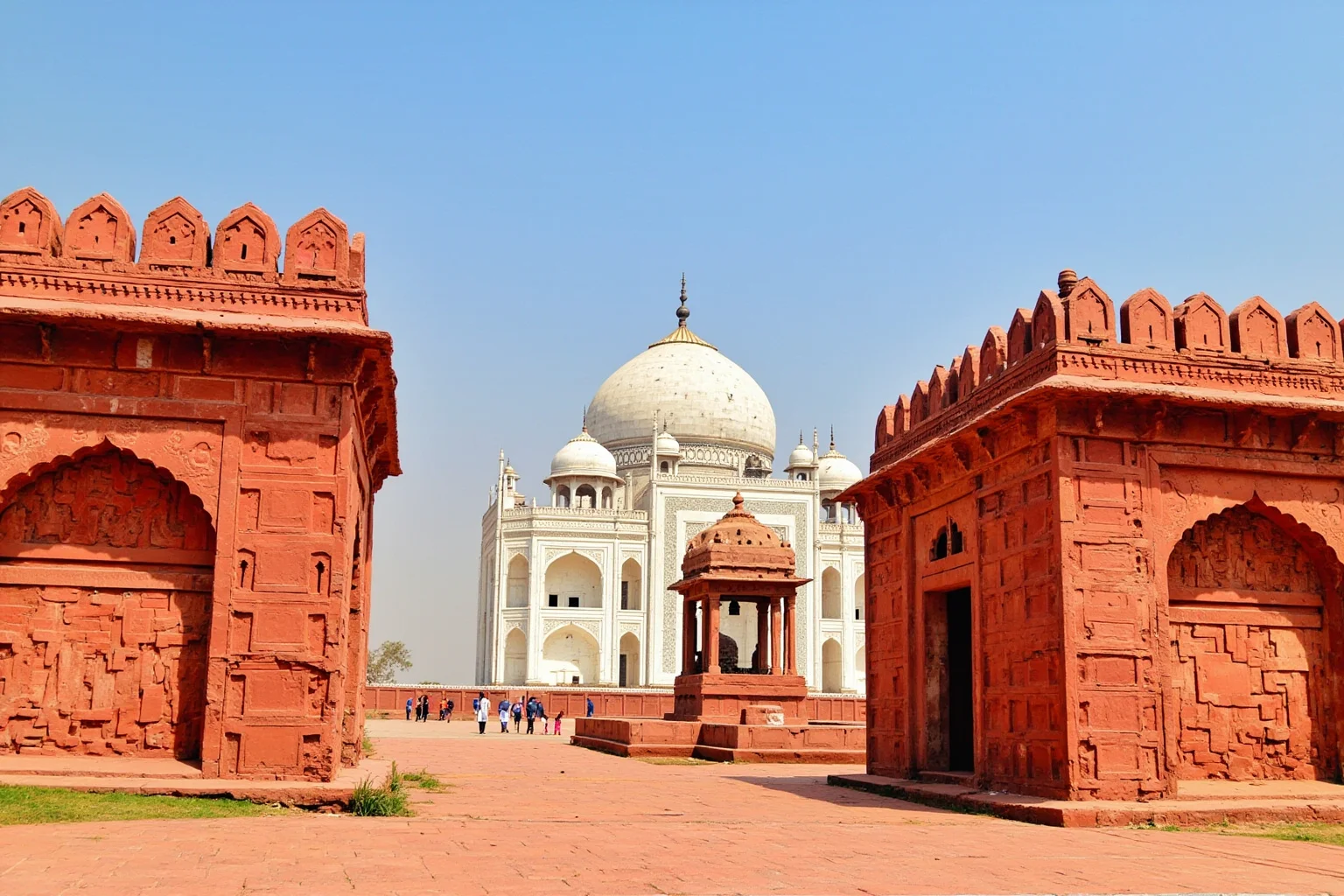 Two matching red sandstone buildings flanking a white marble mausoleum, one shown as a mosque with a prayer niche