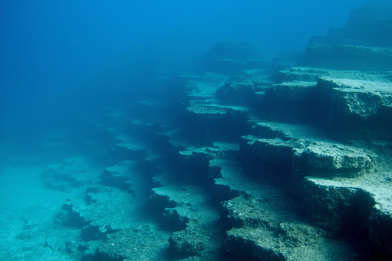 22 Ocean Mysteries We Still Haven't Solved 11 Underwater rock terraces with sharp geometric edges resembling stepped pyramid ruins beneath clear blue water