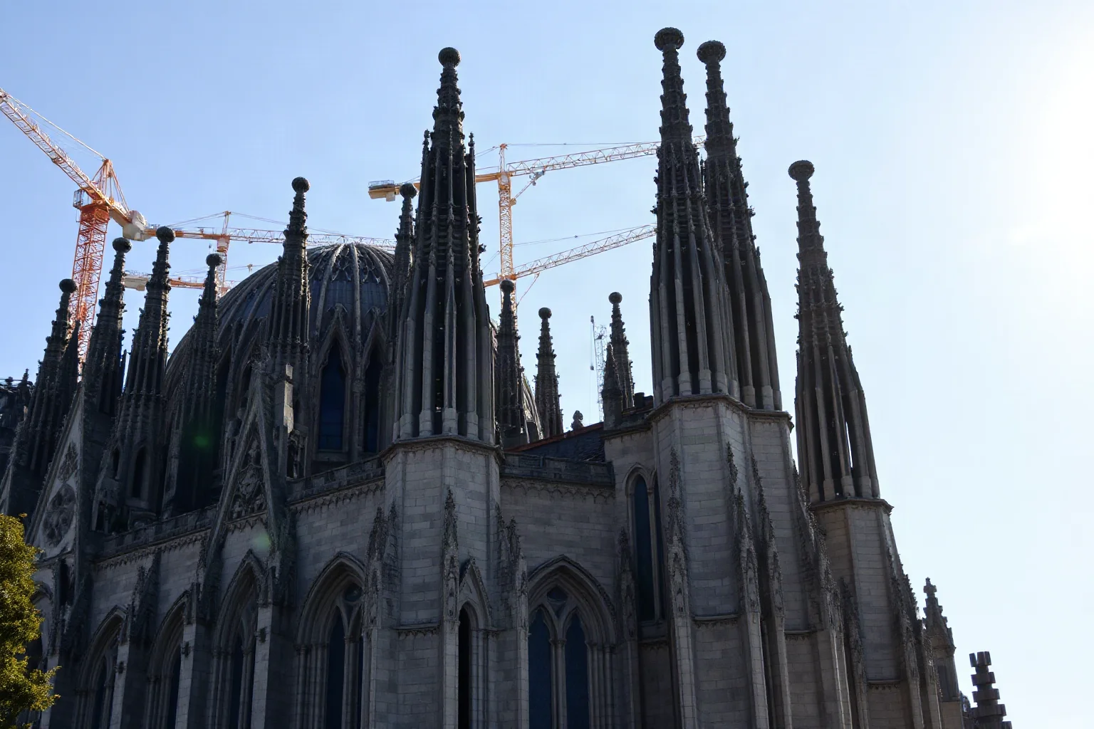 Unfinished organic-shaped cathedral with tall spires and intricate stonework, construction cranes faintly visible, sunny day