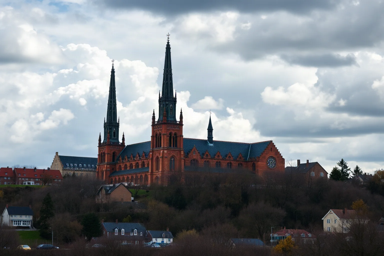 Victorian Gothic Revival cathedral with three tall spires on a hilltop town, dramatic clouds, wide landscape shot