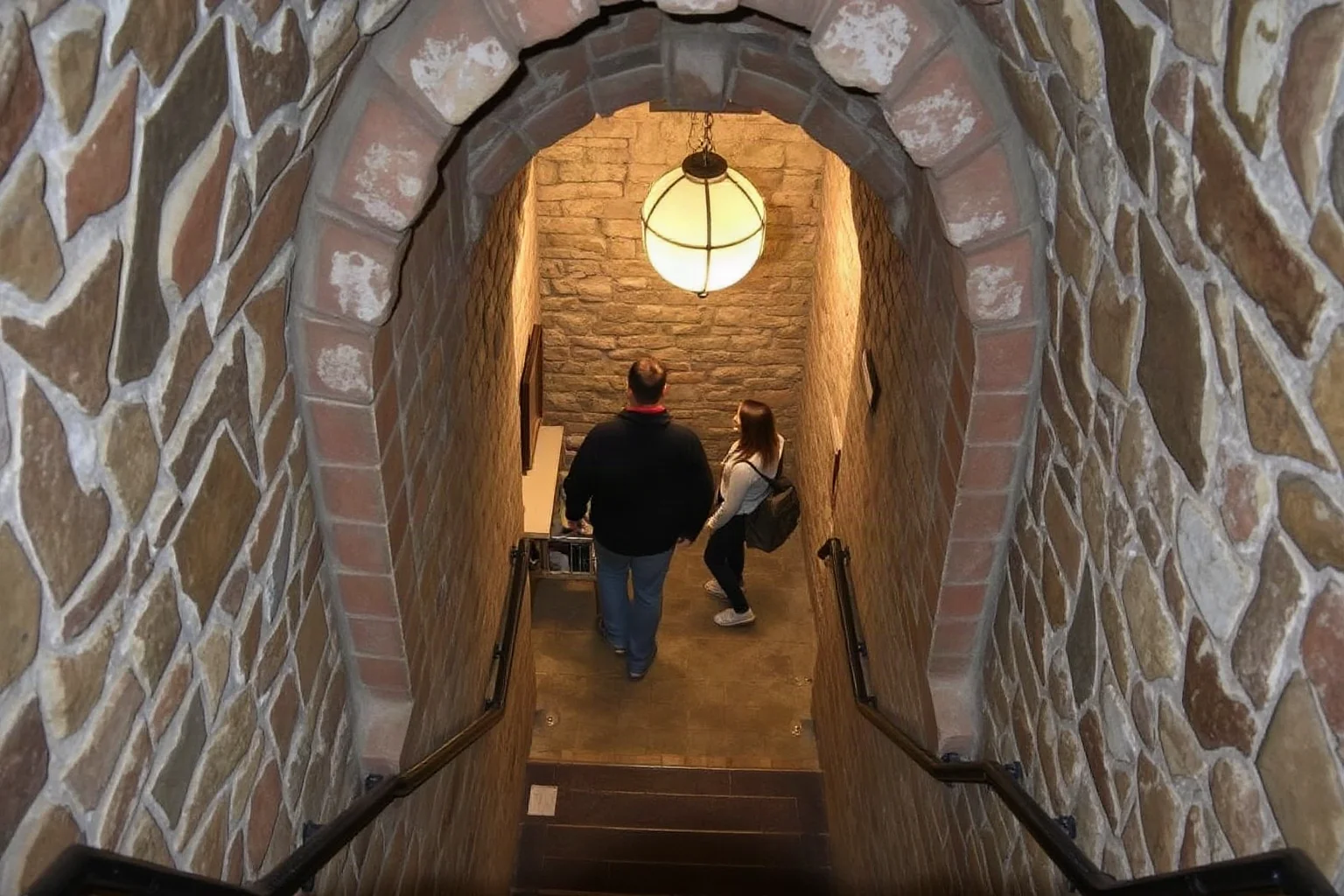Visitors descending narrow stone stairs with handrails into an underground ossuary museum entrance