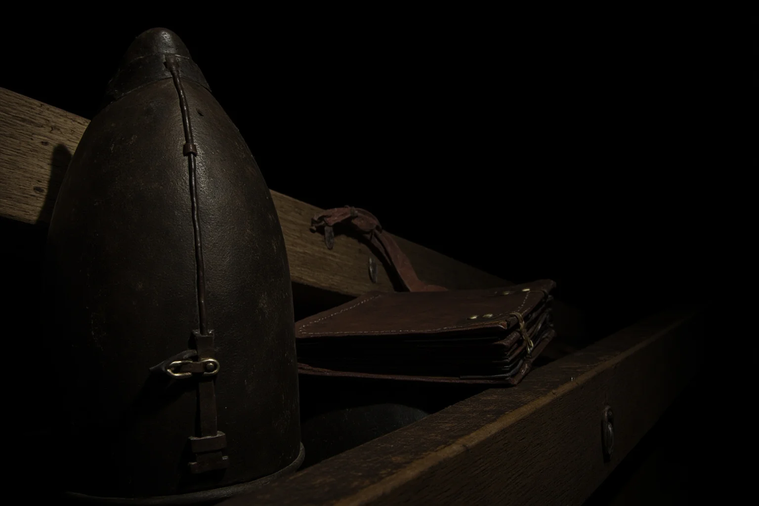 Best Nonfiction Books About WWI: The 25 Best WWI and WWII Reads 5 Weathered leather journal and helmet resting on a wooden trench beam, moody lighting