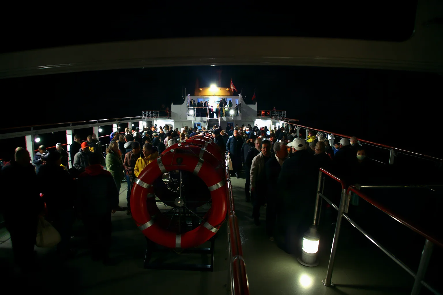 Wide shot of an ocean liner's deck at night, crowded with passengers far outnumbering the available lifeboats