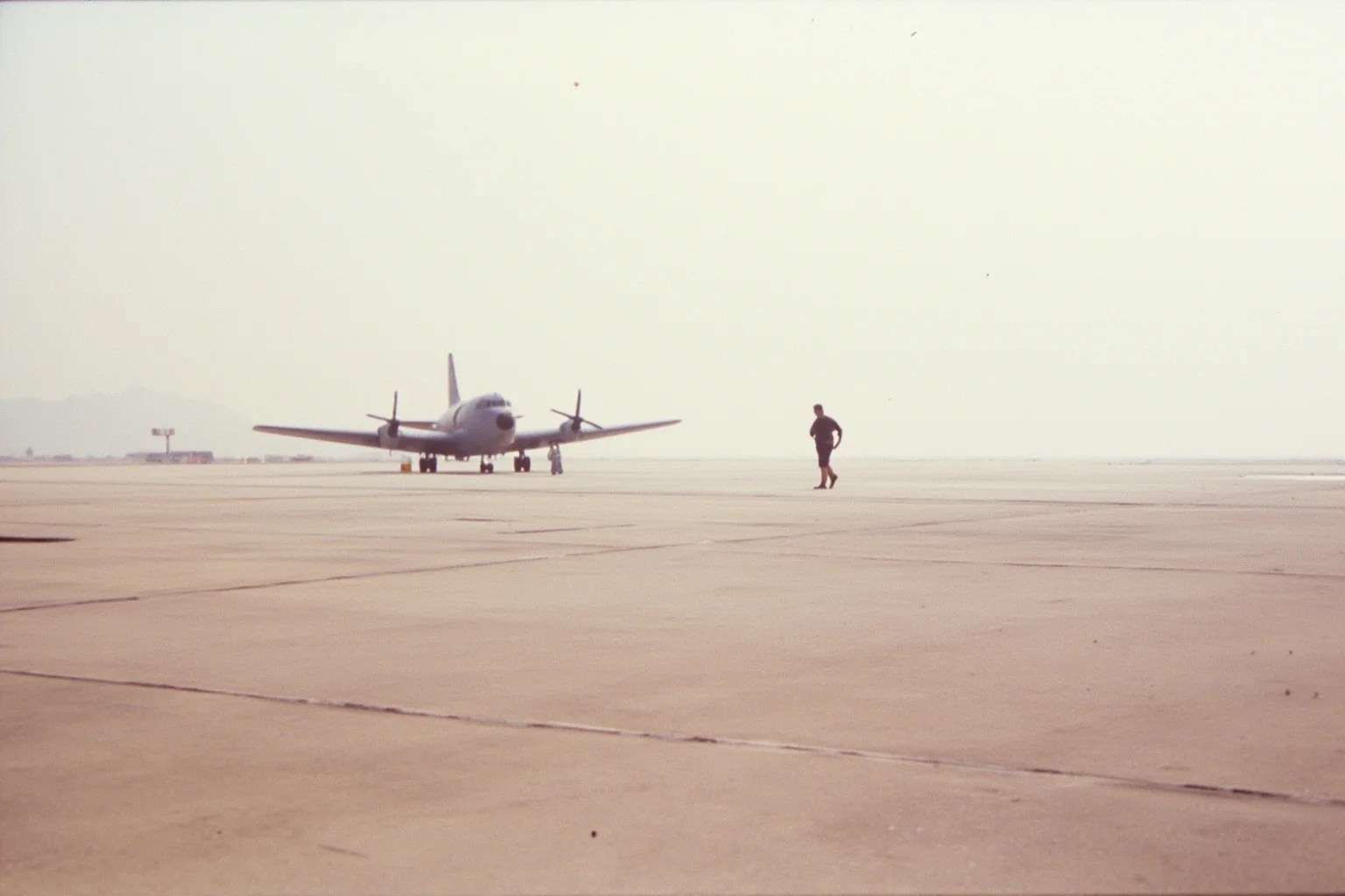 22 Evil Dictators Who Were Eventually Overthrown 12 A 1970s airport tarmac with a military plane and a lone figure boarding in the distance, dusty scene.
