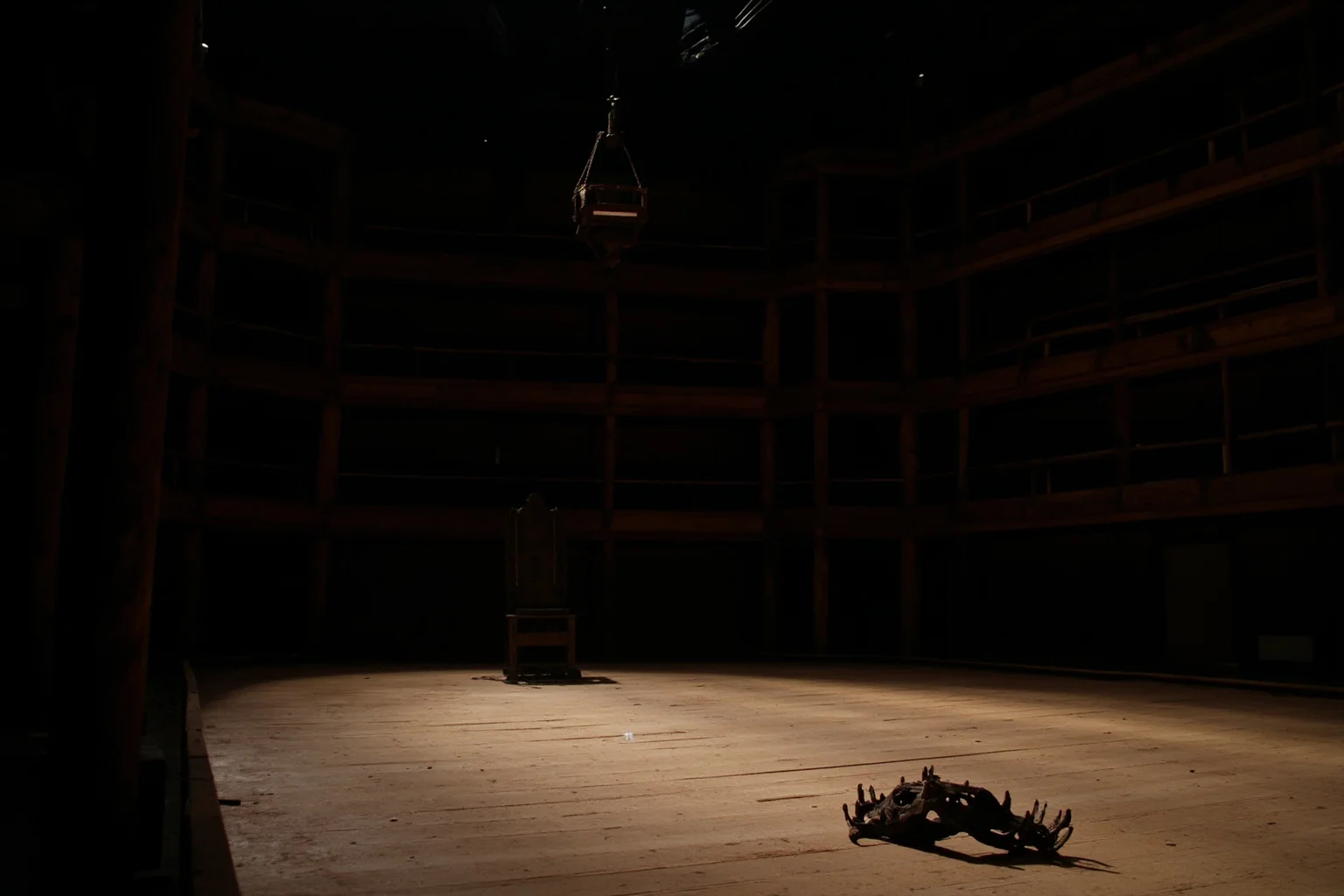 A bare wooden stage in an Elizabethan playhouse with a single throne and a fallen crown under harsh light, empty galleries, dramatic chiaroscuro.