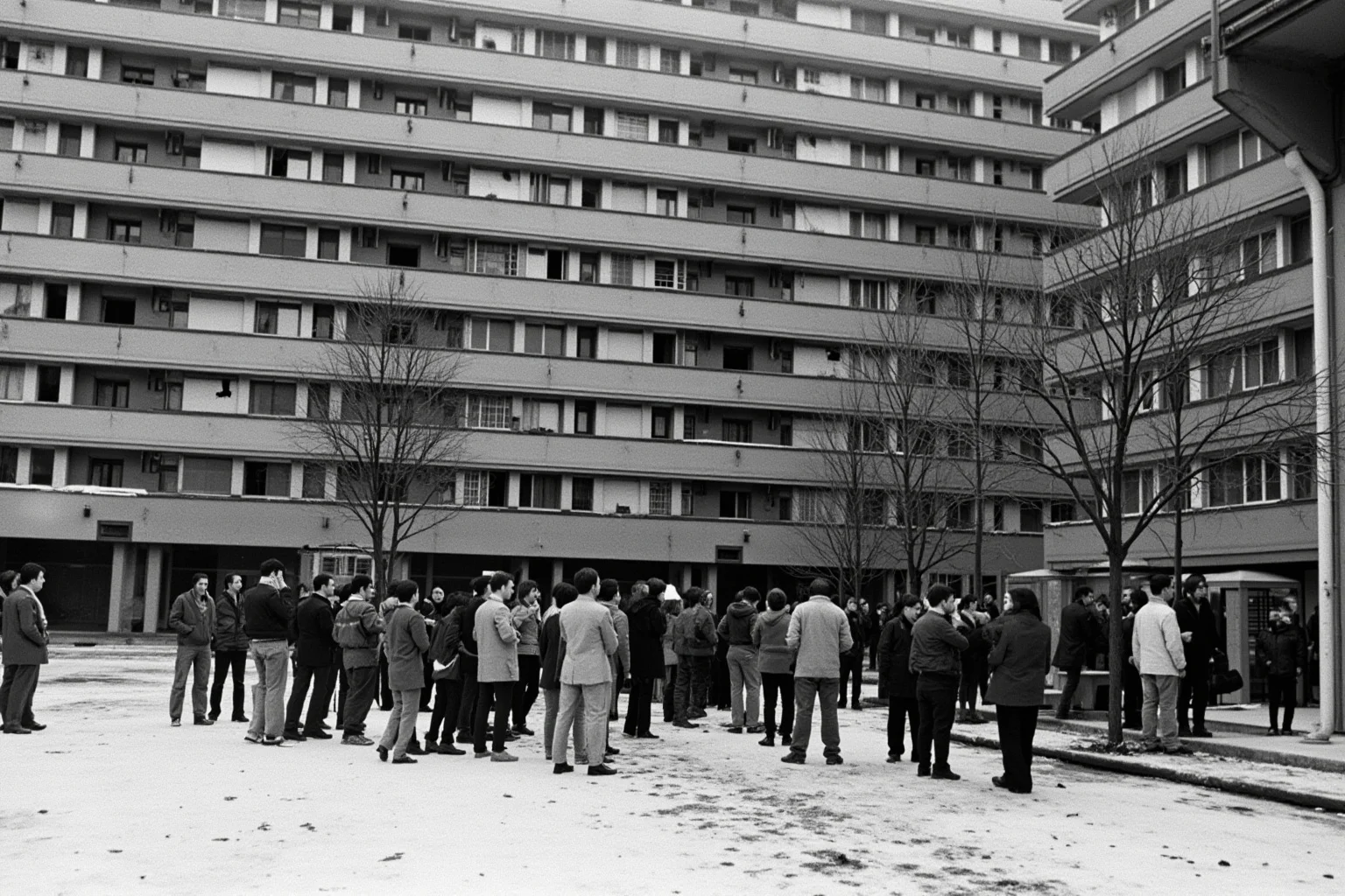 22 Evil Dictators Who Were Eventually Overthrown 10 A bleak 1980s Eastern European apartment block with a crowd gathering, snow on the ground, gray tones.