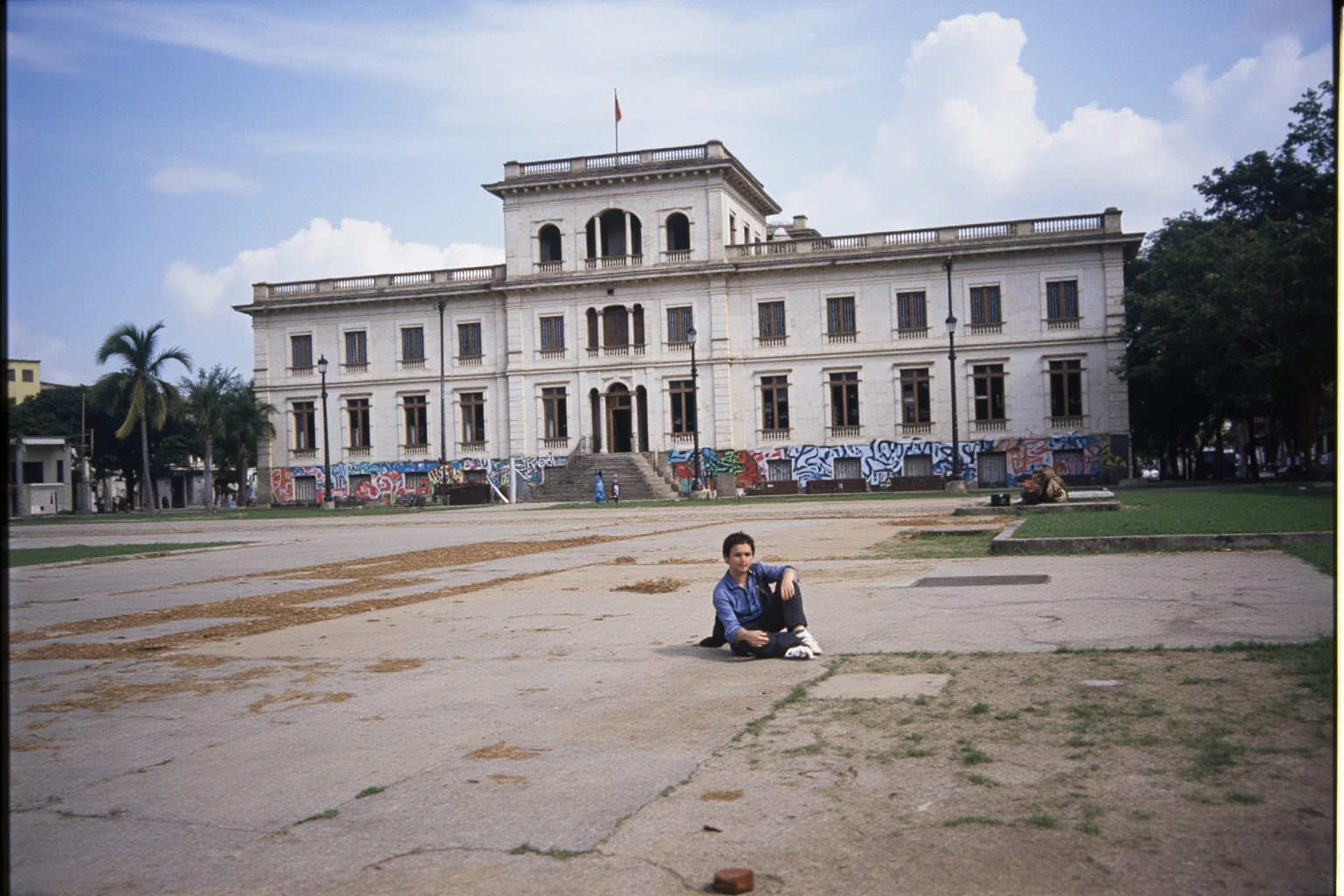 22 Evil Dictators Who Were Eventually Overthrown 9 A Central American plaza with a crumbling presidential palace and revolution graffiti, 1970s atmosphere.