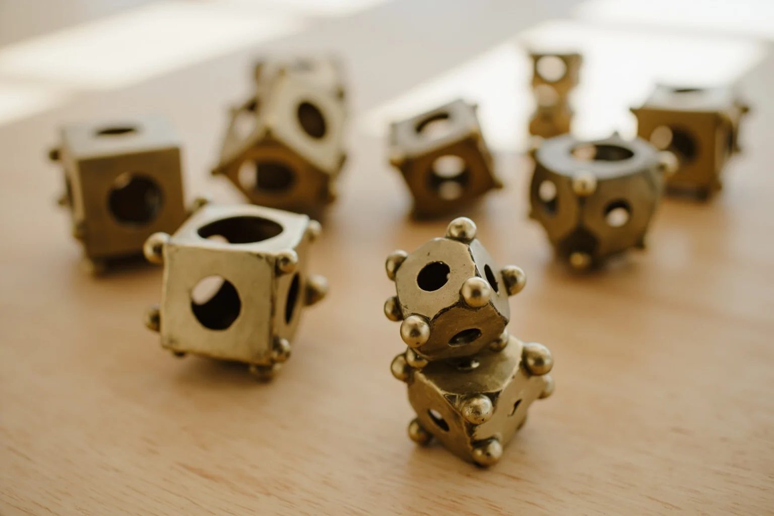 A collection of small hollow bronze dodecahedra with circular holes of varying sizes and knobs at the corners, arranged on a wooden table, soft natural light.