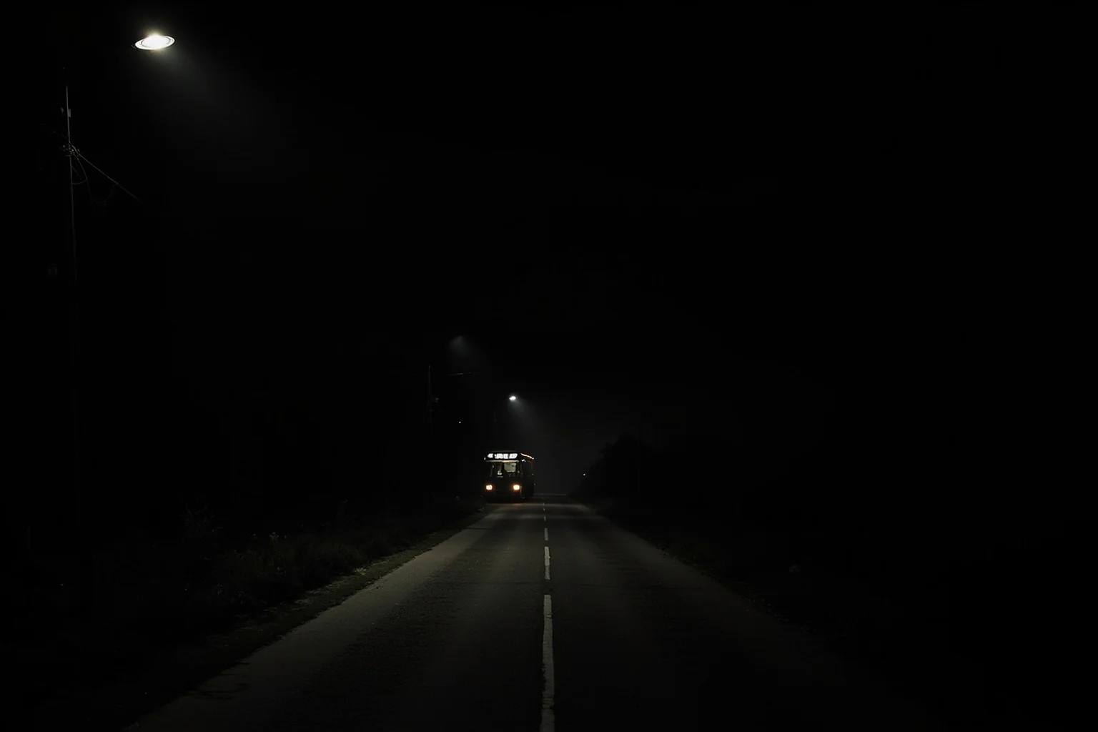 A dark rural road at night with a single bus station light, suspenseful historical mood, no people.