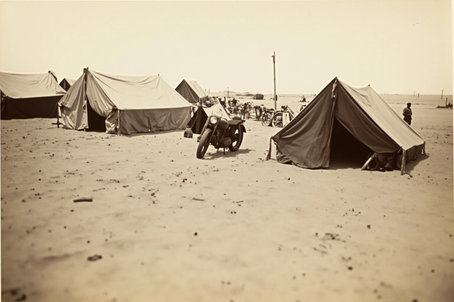 A desert encampment in the Middle East with tents and a vintage motorcycle, early 20th century, no people visible.