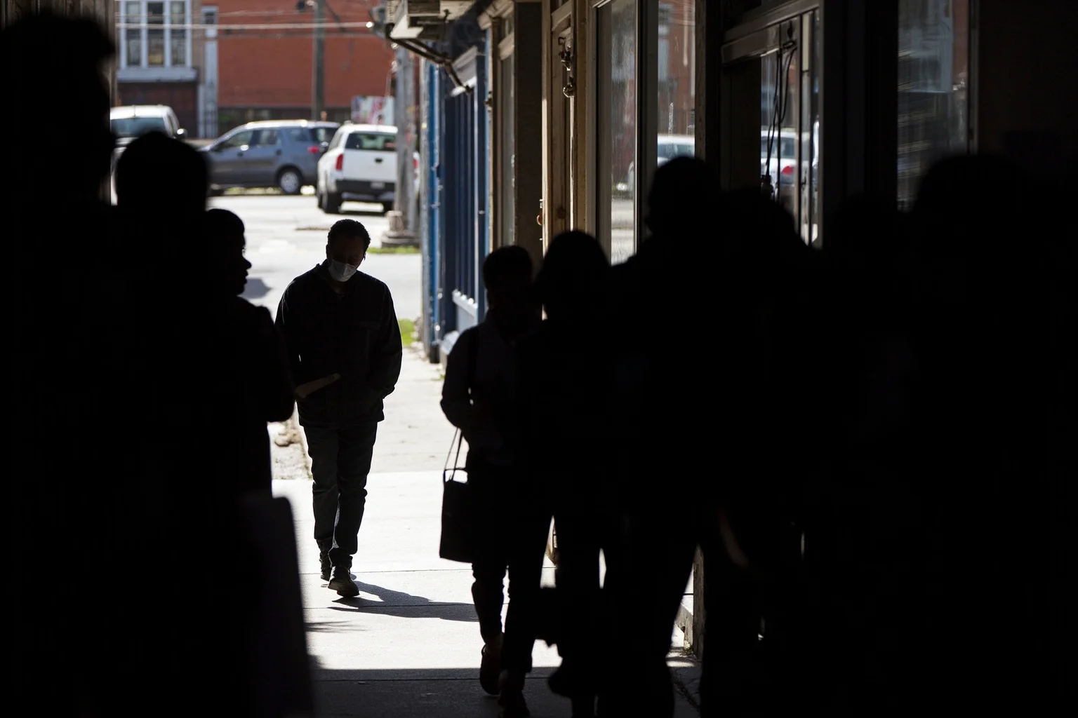A dramatic silhouette of a man walking down a segregated sidewalk while hostile figures stare, faces blurred, no identifiable person.