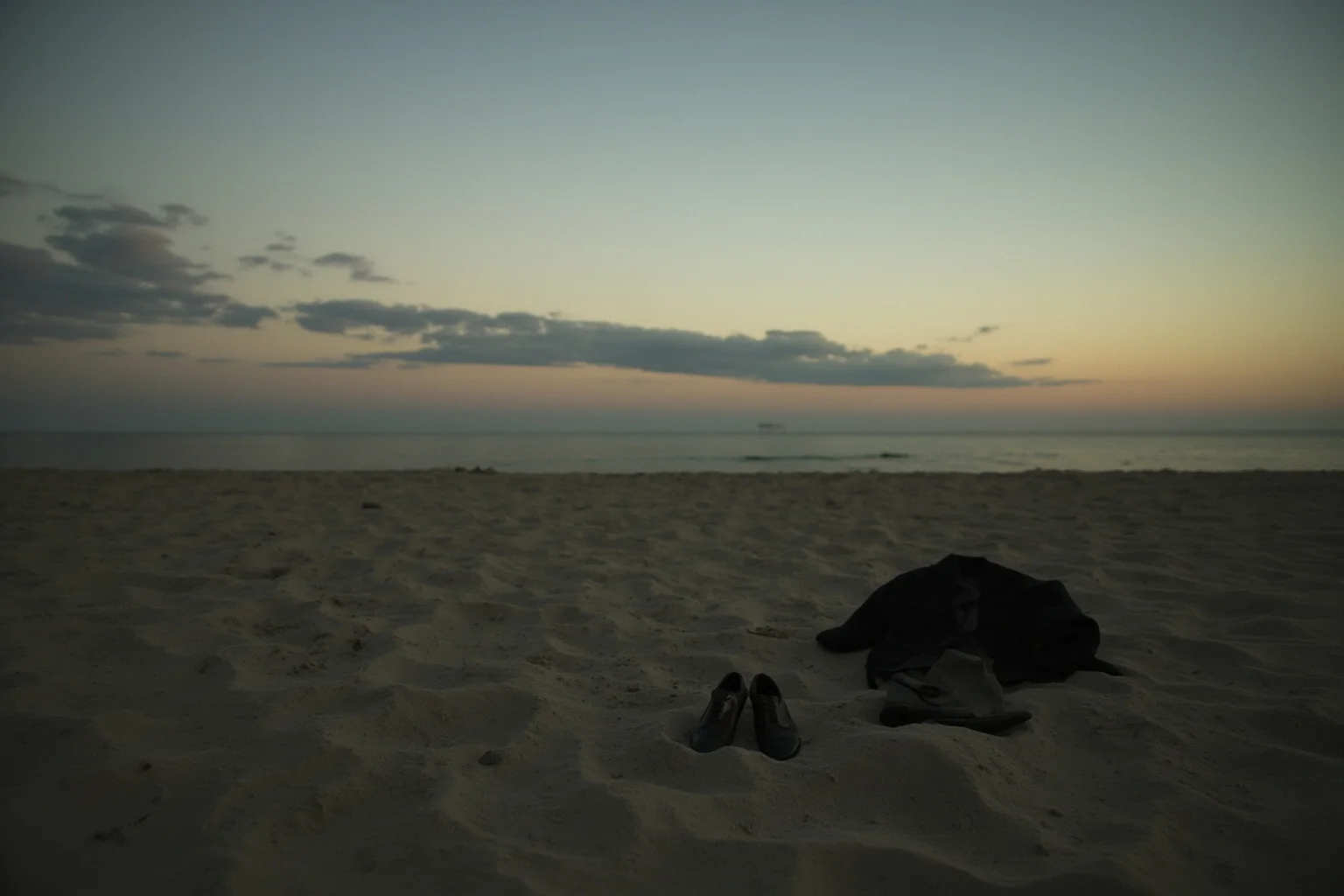 A lonely beach at dusk in 1940s South Australia, a single abandoned suit jacket and shoes on the sand, no people