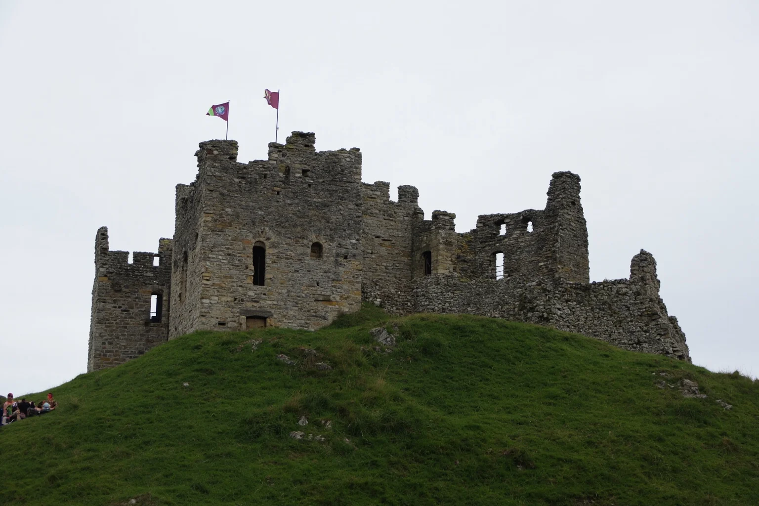A medieval Norman castle on a hill with banners and a stone keep, overcast sky, no people visible.