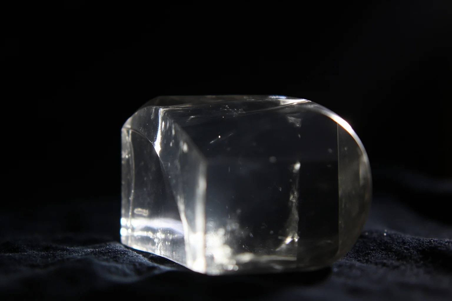 A polished rock crystal lens with a convex shape, resting on a velvet cloth, with a beam of light passing through it, studio lighting.