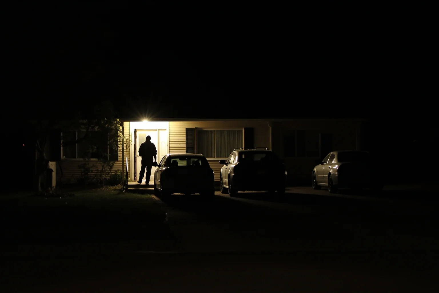Scariest Missing Persons Cases in History: 20 Creepy Disappearances That Still Baffle Us 8 A quiet suburban house at night with a broken porch light, three cars in the driveway, an open front door, unsettling stillness, no people.