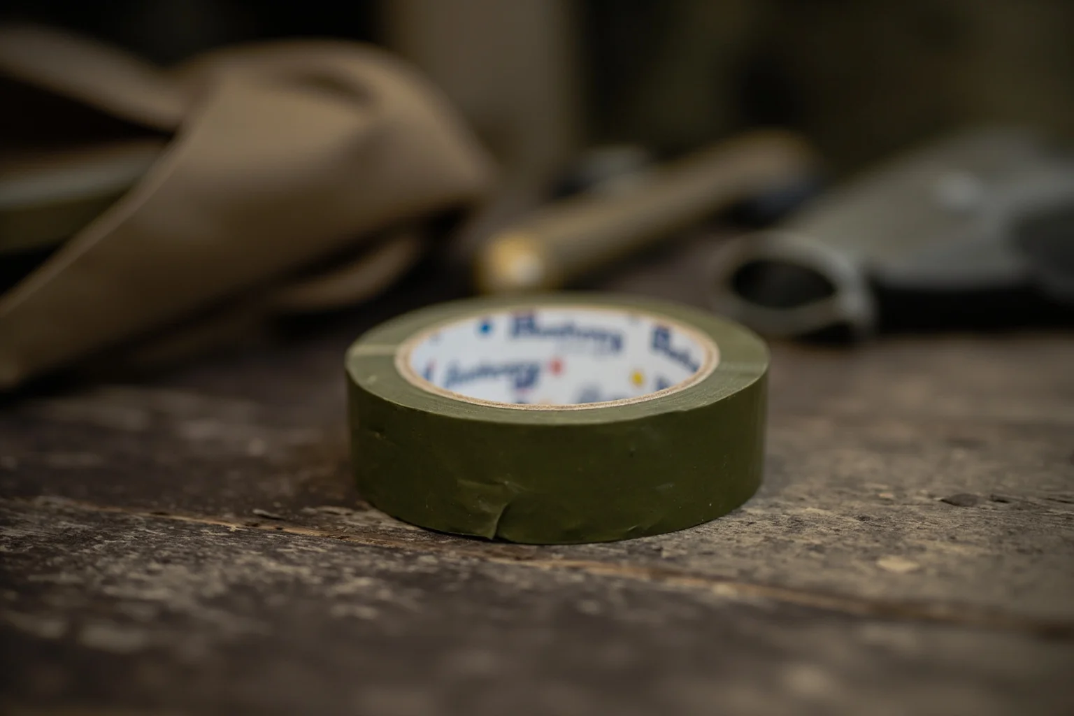 A roll of olive-drab duct tape on a wooden table with military supplies, 1940s still life